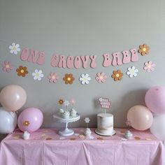 a table topped with cake and balloons next to a sign that says, one baby