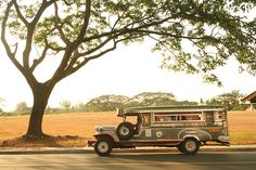 an old jeep is parked on the side of the road in front of a tree