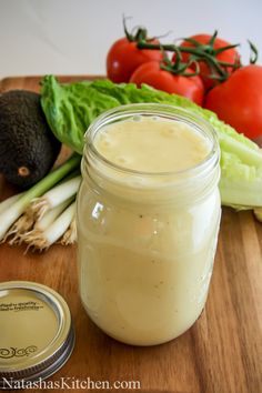 a wooden cutting board topped with a mason jar filled with liquid next to tomatoes and lettuce