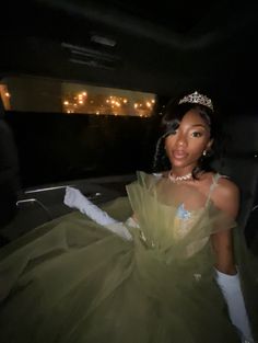 a woman in a green dress and tiara is sitting in a car at night