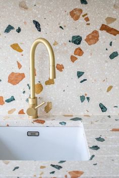 a white sink sitting under a faucet next to a wall covered in multicolored tiles