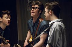 three young men standing next to each other in front of microphones and guitar strings