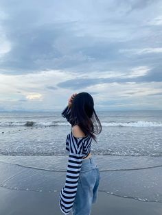 a woman standing on top of a beach next to the ocean holding onto her hair