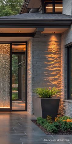 the entrance to a modern house with large plants and lights on it's side