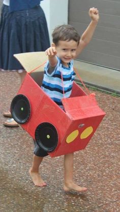 a young boy is holding up a cardboard box shaped like a race car with wheels