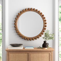 a round mirror on the wall above a wooden dresser with a vase and plant in it