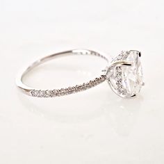 a white gold ring with an oval cut diamond and pave set diamonds on the band