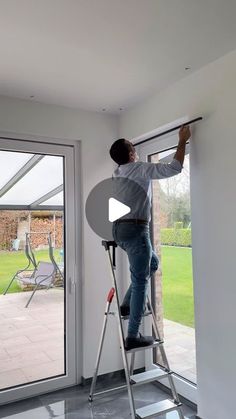 a man standing on a stepladder in front of a sliding glass door while painting the wall