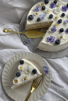 a piece of cake with blueberries and flowers on it sitting next to a fork