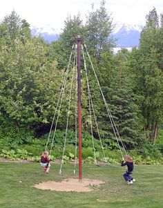 two children are playing on a swing set in the grass with trees and mountains in the background