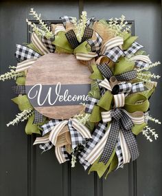 a welcome wreath with green and white ribbons hanging on the front door, decorated with greenery