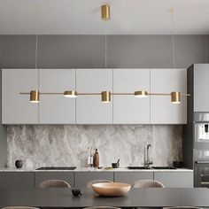 a modern kitchen with marble counter tops and white cabinets, along with gold pendant lights