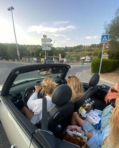 people sitting in the back seat of a convertible car with beer bottles on the backseat