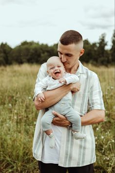 a man holding a baby in his arms while standing in a field with tall grass