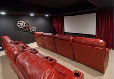 an empty theater room with red leather couches and projector screen in the corner