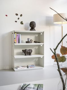 a white shelf with books and figurines on it next to a vase filled with flowers