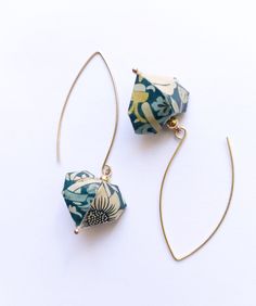 two pairs of earrings are shown on a white surface, one is blue and the other is gold