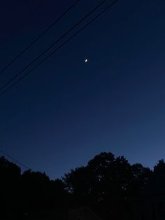 the moon is shining brightly in the dark blue sky above some houses and power lines