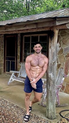 a shirtless man standing in front of a log cabin