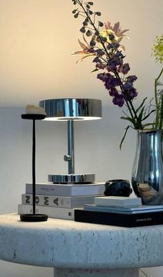 a vase with flowers and books on a table next to a wall light that is turned on