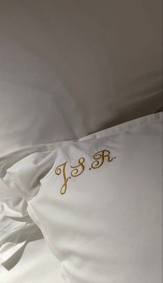 the monogrammed pillow is on top of the white bedding with gold lettering