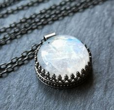 The gorgeous moonstone in this necklace glows with its own internal light, reflecting blue flashes. The simple round shape of the stone is reminiscent of a shining full moon. The 16mm stone is held in a patterned sterling silver bezel setting, open on the back to let in extra light and to show off the gorgeous colors reflected on the back of the stone. The pendant is hung on a sterling silver chain, available in your choice of 16, 18, or 20 inches. The necklace has been oxidized and brushed, giv Ethereal Moon Phase Jewelry For Gift, Handmade Celestial Crystal Necklace, Mystical Round Moonstone Jewelry, Mystical Moonstone Round Pendant Jewelry, Round Moonstone Necklace With Moon Charm, Magical Round Moonstone Jewelry, Magical Moonstone Moon Phase Jewelry, Ethereal Moonstone Jewelry As A Gift, Ethereal Moonstone Jewelry For Gift