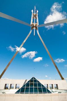 an artistic sculpture in front of a building with blue sky and white clouds above it