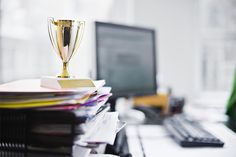 a stack of files and a trophy on top of a desk in front of a computer