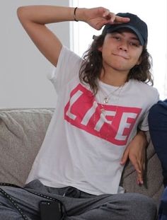 a young man sitting on top of a couch wearing a hat and holding his hand to his head