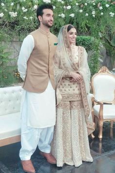 a man and woman standing next to each other in front of a flower covered wall