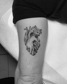 a black and white photo of two hands holding a rose tattoo on the left arm