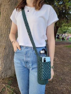 a woman holding a cell phone in her hand and wearing a crocheted bag