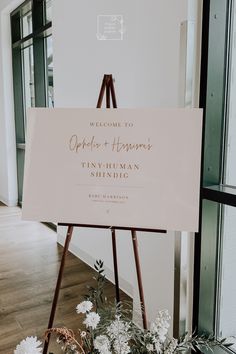 a welcome sign with flowers in the foreground and an easel on the floor