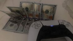 a video game controller and money sitting on top of a white table next to a pile of cash