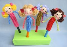 four crocheted dolls standing on top of a green stand with sticks in each hand