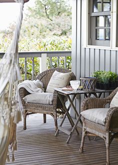 two wicker chairs sitting on a porch next to a table and hammock