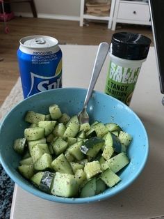 a blue bowl filled with cucumbers next to a can of soda and a computer