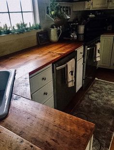 a kitchen with wooden counter tops and white cabinets, along with an old style dishwasher