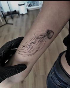 a person with a black glove on their arm holding a small jellyfish in the water