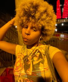 a woman with an afro is listening to music on her headphones while standing outside at night