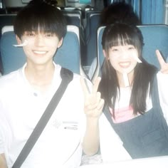 two people sitting on a bus with one holding up the peace sign and the other pointing at the camera