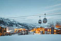 the ski lift is hanging over the town at night in the snow covered mountain range