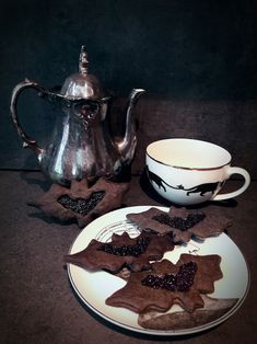 a plate with some cookies on it next to a silver tea pot and saucer