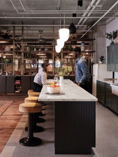 two people are standing at the counter in an industrial style kitchen with marble counters and stools