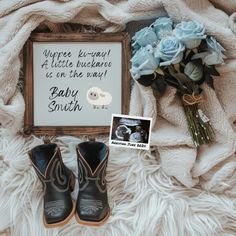 a baby announcement with booties and flowers on a blanket next to a framed sign