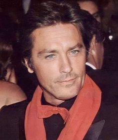 a man in a tuxedo and an orange scarf is looking at the camera