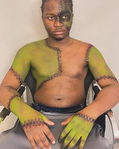 a man with green paint on his body sitting in a chair