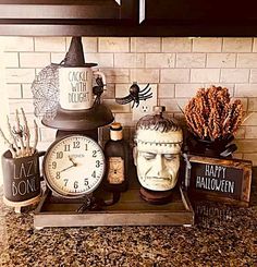 an assortment of halloween decorations on a kitchen counter with a clock, candles and other items