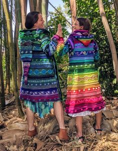 two women in colorful dresses standing next to each other on the ground with trees behind them