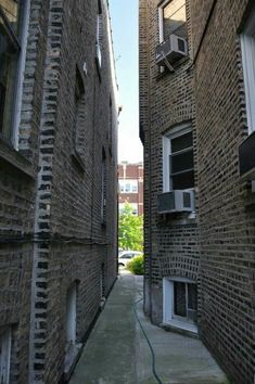 an alley way between two buildings with brick walls and windows on each side, looking up at the sky